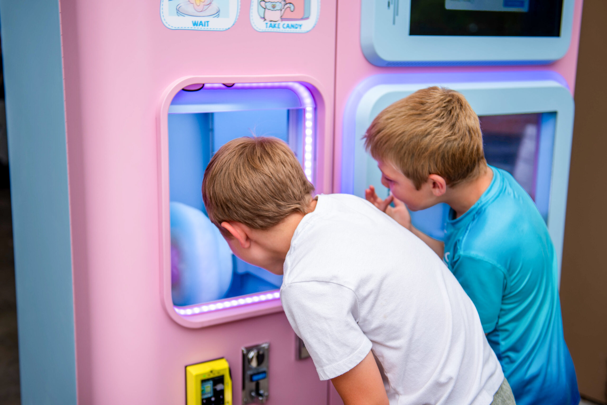 Two children watching cotton candy being dispensed from a cotton candy machine with wonder and excitement